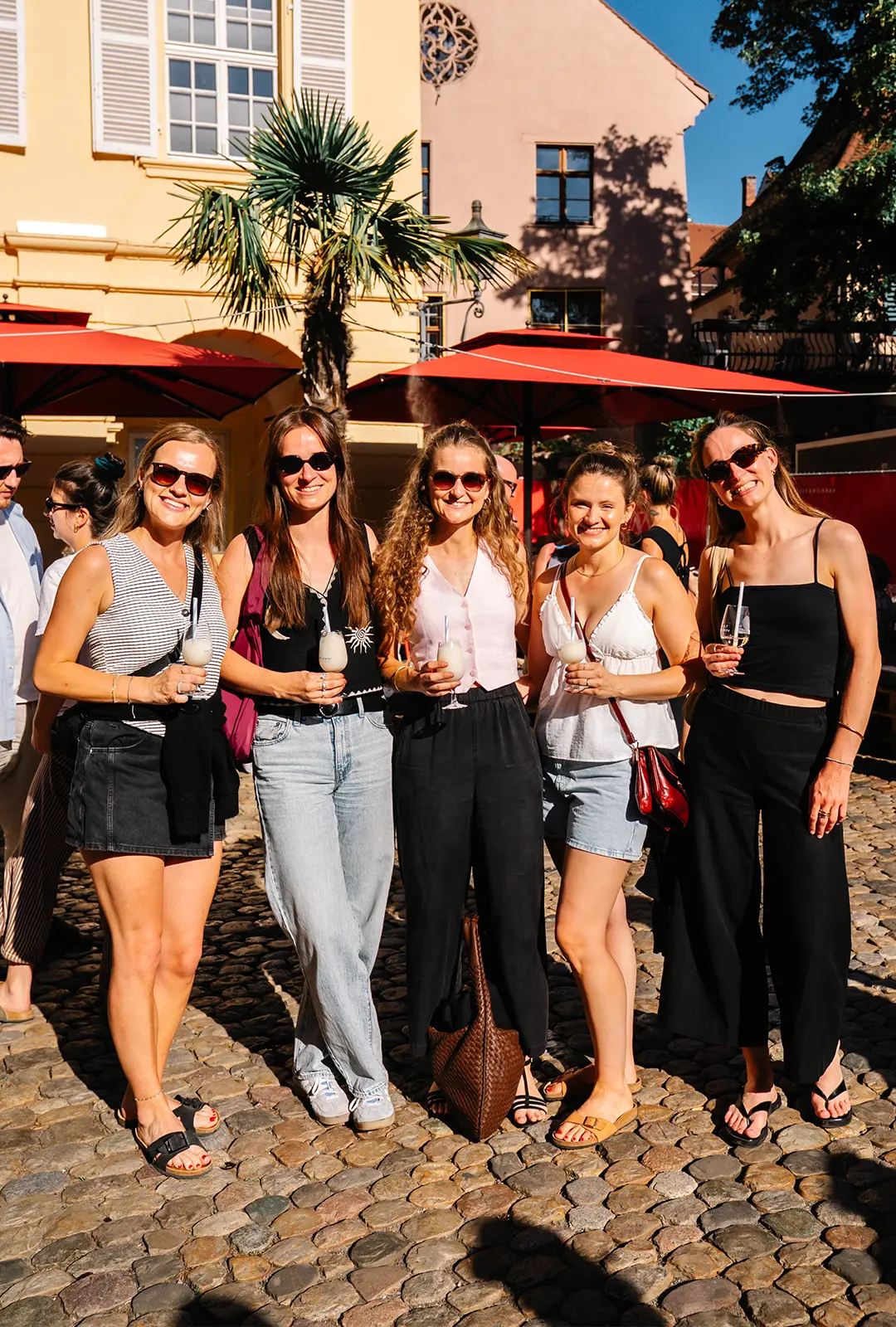 Eine Gruppe Frauen posiert vor der Alten Wache in Freiburg, jede mit einem Glas „Kalte Sofie" in der Hand, an einem strahlenden Sommertag.
